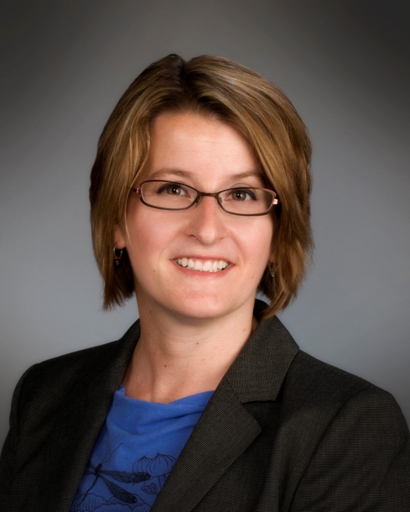 A professional looking but smiling headshot of a white middle aged woman with shoulder length light brown hair and glasses. She is wearing a blazer with a blue tshirt underneath. 